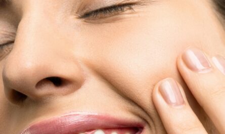 A close-up portrait of a joyful woman with closed eyes, pink lipstick, and her hand touching her cheek.