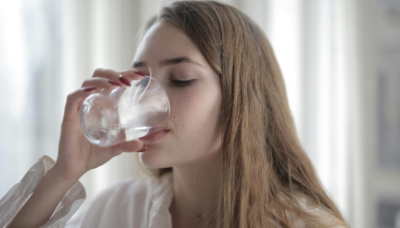 A woman enjoying a refreshing glass of water indoors during the day.